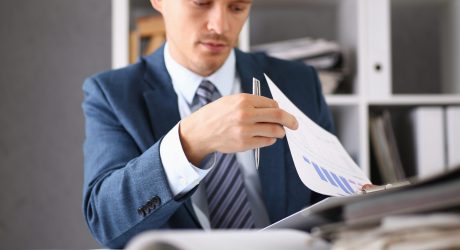 Serious businessman in the office examines documents Serious businessman in the office examines documents with infographics performing assigned work holds a pen in hand near a ballroom is extremely concentrated think thinker